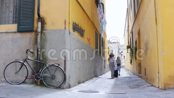 两个年轻的旅行快乐的女人带着行李走在黄色的墙壁上视频的预览图