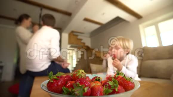 盛满成熟草莓的碗和模糊的家庭成员吃浆果手持视频的预览图