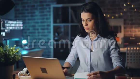 晚上在办公室工作的漂亮女孩微笑着在笔记本上写字视频的预览图