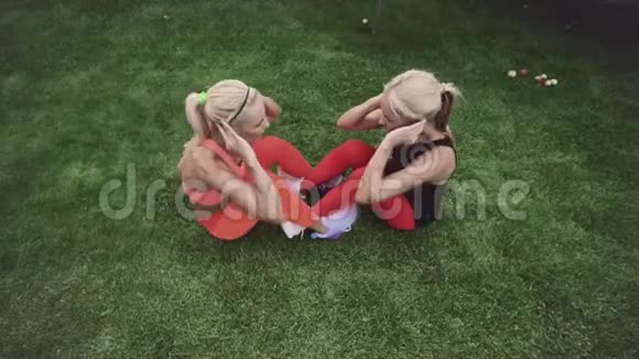 两个金发碧眼的双胞胎姐妹在绿草上做体育锻炼夏日阳光明媚俯视图视频的预览图