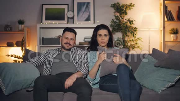 一对漂亮的夫妇坐在家里的沙发上看恐怖片视频的预览图