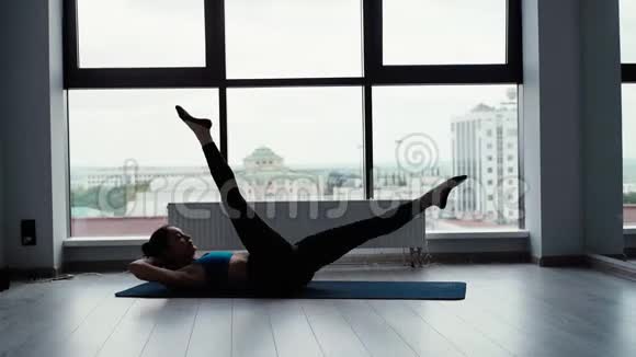 灵活的年轻女子躺在运动垫上缓慢地抬起双腿视频的预览图