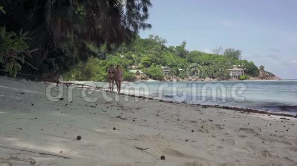 塞舌尔普拉斯林岛两个穿着泳衣的苗条可爱的女孩走在令人惊叹的岛屿海滩上和视频的预览图