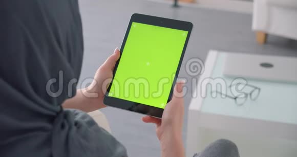穆斯林女商人戴着头巾手里拿着带有绿色彩色屏幕手表的平板电脑坐在办公室里视频的预览图