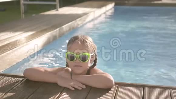 画像上戴着黄色太阳镜的漂亮有趣的女孩微笑着看着镜头望着游泳池外抓住视频的预览图