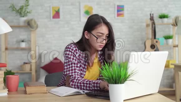 漂亮的亚洲女孩在家里的客厅里坐在桌旁拿着笔记本电脑学习视频的预览图
