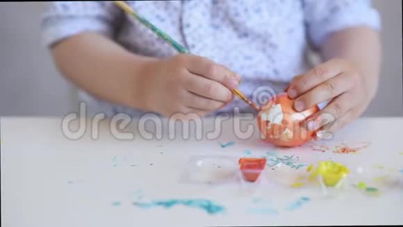 一个小小孩用画笔在桌子上画一个橙色的复活节彩蛋视频的预览图