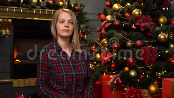 一个坐在圣诞树旁的漂亮金发女郎送礼物视频的预览图