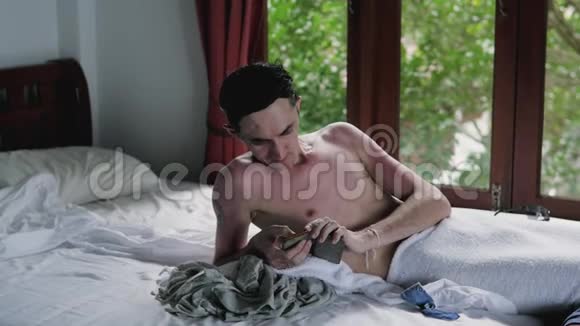 淋浴后的人躺在床上靠窗户的电话可以俯瞰花园一个男人躺在床上视频的预览图