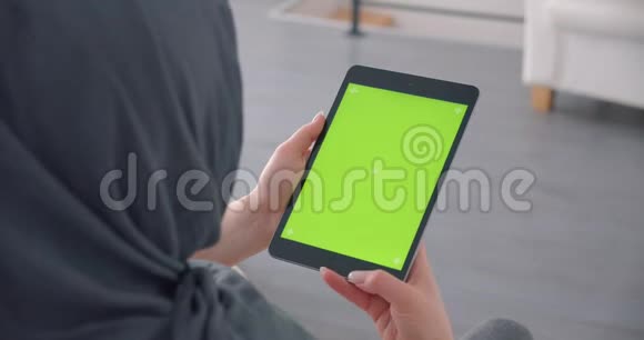 戴着头巾的穆斯林女商人在平板电脑上聚精会神地看着办公室里坐着绿色的彩色屏幕视频的预览图