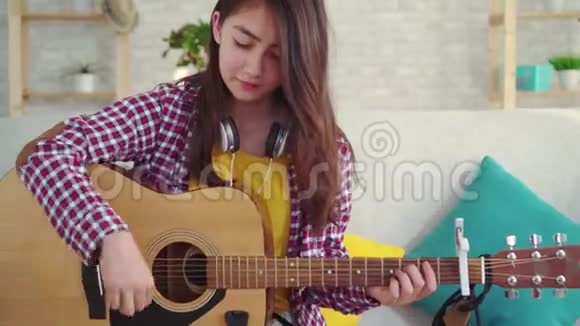 漂亮的亚洲女孩在房子的客厅里拿着吉他看着相机微笑视频的预览图