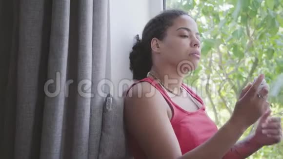 漂亮的非裔美国女人坐在窗台上特写那个女孩脸上喷着化妆品视频的预览图