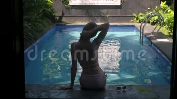 一位美丽的年轻女子穿着泳衣留着长发坐在一个豪华度假胜地的游泳池附近女孩系领带视频的预览图