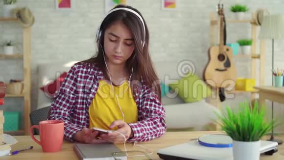 美丽的亚洲女孩留着长发坐在现代化的客厅里带着耳机听音乐放松身心视频的预览图