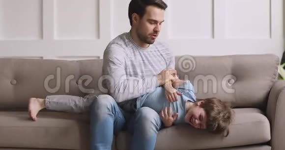 快乐的爱爸爸挠痒痒的孩子儿子笑着在沙发上玩耍视频的预览图