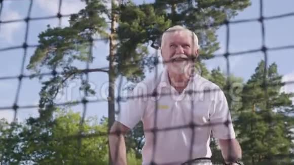 在网球场上打网球的快乐快乐微笑的成熟男人老人用球拍扔球视频的预览图
