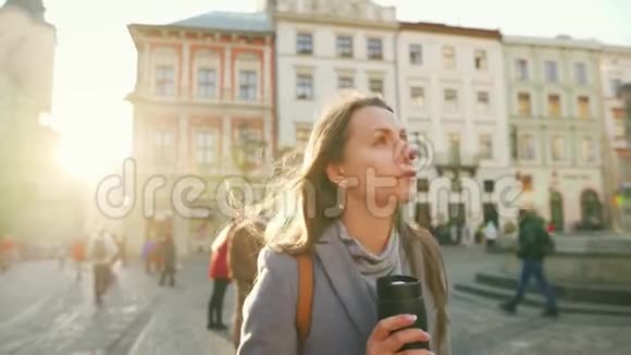 女人手里拿着一个保温杯走在街上欣赏日落时分的古城建筑视频的预览图