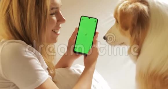 绿色屏幕跟踪点漂亮女学生的肖像正在使用智能手机显示屏幕笑着躺在床上视频的预览图