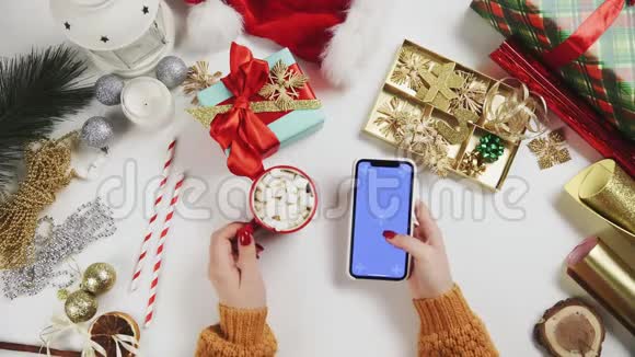 女人喝可可和使用智能手机与Chroma键敲击滚动白色圣诞假日装饰视频的预览图