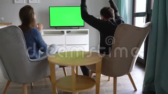 男人和女人坐在椅子上用绿色的屏幕看电视他们情绪激动看体育节目视频的预览图