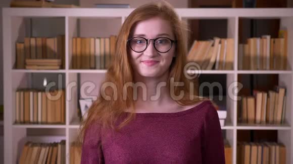 年轻的红头发漂亮的白种人戴着眼镜的女学生的特写肖像在镜头里显示了好的标志视频的预览图