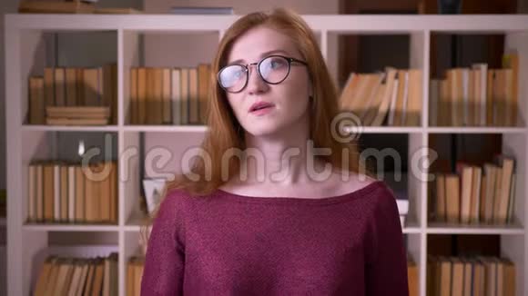年轻的红头发迷人的白种人戴眼镜的女学生的特写肖像使一张脸被激怒和手掌视频的预览图