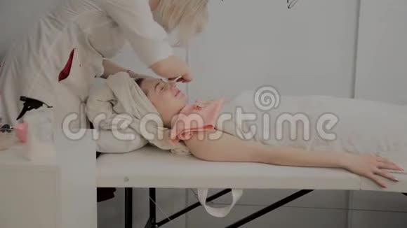 一位专业的美容师用特殊的保湿湿巾擦女孩的脸美容学的新概念视频的预览图