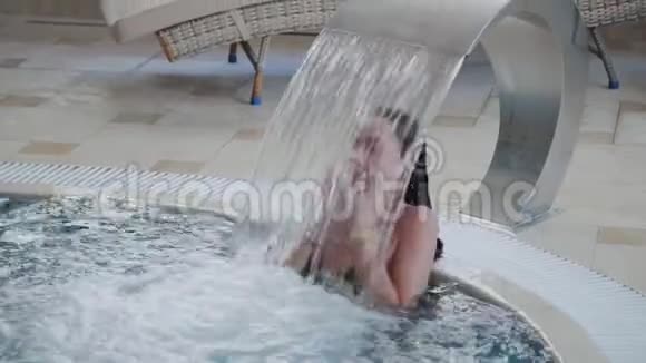 美丽的女孩在室内游泳池的瀑布下游泳视频的预览图