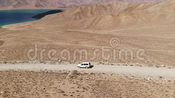 在4x4路的一侧汽车沿着砾石小径驶向干旱山区的湖泊帕米尔公路丝绸之路视频的预览图
