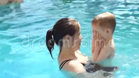 一位快乐的母亲在游泳池里游泳时拥抱她儿子的肖像视频的预览图
