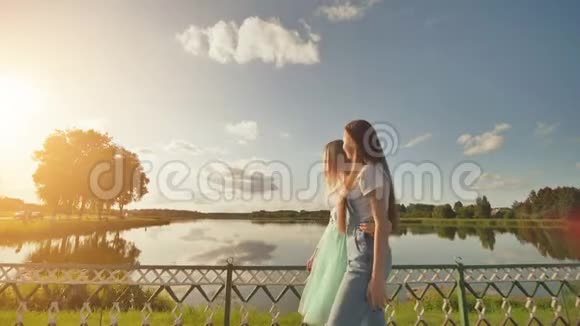 两个姐妹站在一起拥抱在一个美妙的夏日日落和湖泊的背景下录像在移动视频的预览图