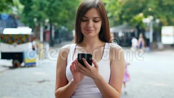 美丽的年轻女子在街上用电话打字视频的预览图