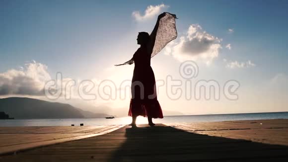 日出时一个戴着围巾的漂亮女人慢吞吞地站在海滨视频的预览图
