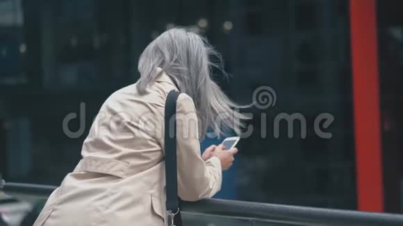 穿着时髦外套的灰发女人站在市中心的扶手附近视频的预览图