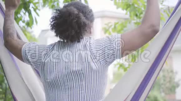年轻的非洲裔美国妇女坐在吊床上在后院放松伸展身体上升视频的预览图