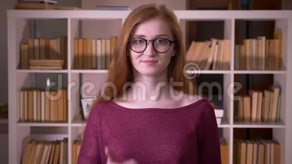年轻的红头发漂亮的白种人女学生戴着眼镜拇指向上微笑着看着视频的预览图