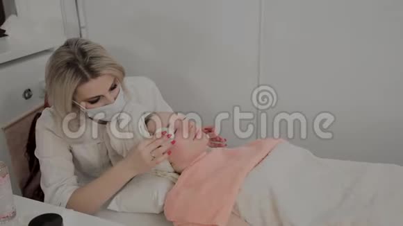 一位专业的美容师用特殊的保湿湿巾擦女孩的脸美容学的新概念视频的预览图