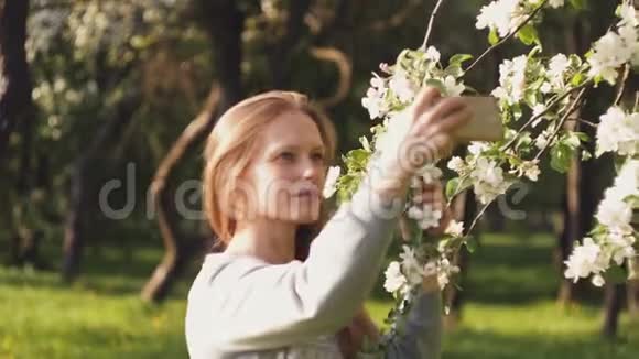 白种人美丽的女孩在开花树的背景下自拍积极的女性背景视频的预览图