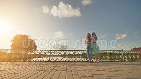两个姐妹站在一起拥抱在一个美妙的夏日日落和湖泊的背景下录像在移动视频的预览图