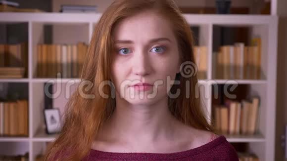 年轻的红头发迷人的白种人女学生在室内的大学图书馆里看着摄像机视频的预览图
