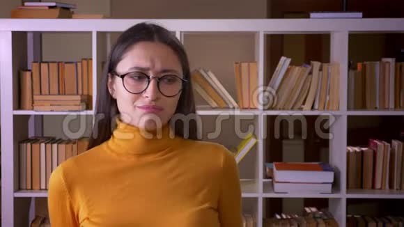 戴着眼镜的漂亮黑发老师的画像把头变成镜头在图书馆里表现出不同意见和拒绝视频的预览图