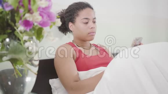 肖像年轻漂亮的非裔美国女人刚醒来她躺在床上发短信与花同放视频的预览图