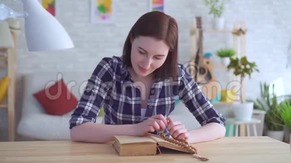 一位年轻女子坐在桌子旁手里拿着念珠正在看书视频的预览图