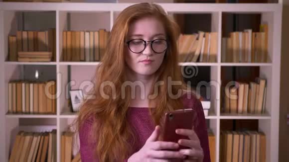 戴眼镜的年轻红发女孩的特写肖像戴眼镜的白种人女学生在手机上打电话视频的预览图