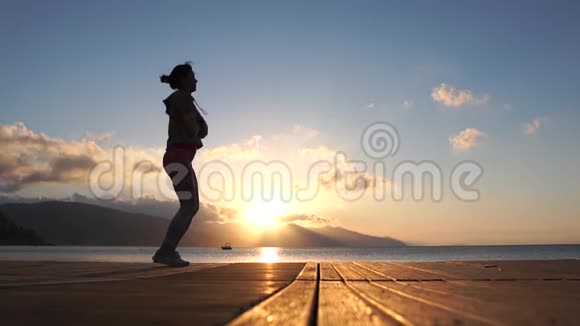 女孩在木制浮舟上训练在日落时缓慢地跳跃视频的预览图