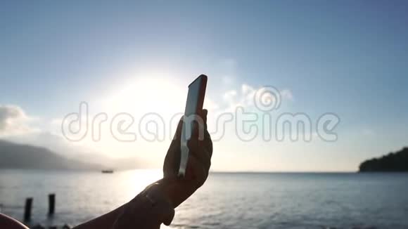 日出时一个女人用智能手机在海面上慢动作视频的预览图