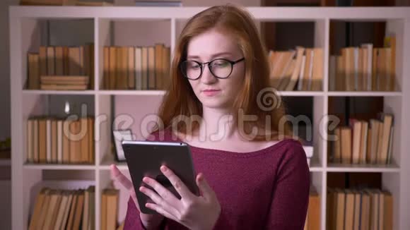 年轻的红头发漂亮的白种人女学生戴着眼镜使用平板电脑并显示绿色视频的预览图
