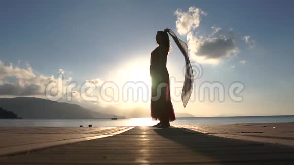 黎明时分一个戴着透明围巾的女人慢悠悠地站在海滨视频的预览图