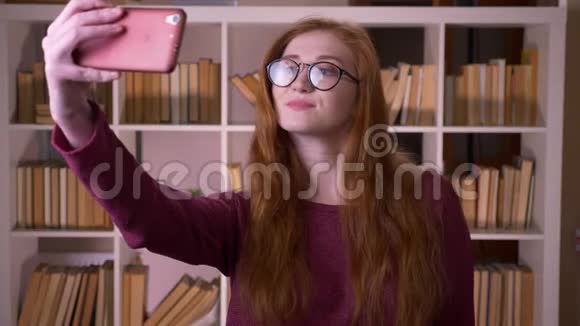 年轻的红头发漂亮的白种人戴眼镜的女学生在电话里自拍视频的预览图