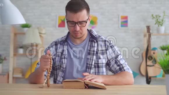 一个戴着眼镜手里拿着念珠读着圣经的年轻人视频的预览图